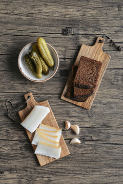 Pork fatback on a wooden cutting board with slices of rye bread, garlic,