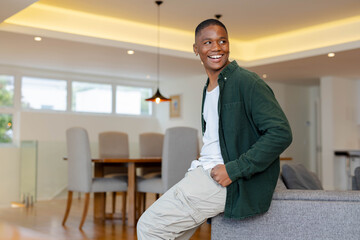 African American man leaning on gray sofa at home wearing dark green overshirt, smiling, copy space