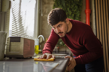 Man intently cleaning kitchen counter with yellow cloth