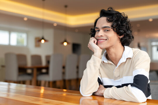 Male wearing striped polo leaning on polished wooden table in modern dining lounge, copy space