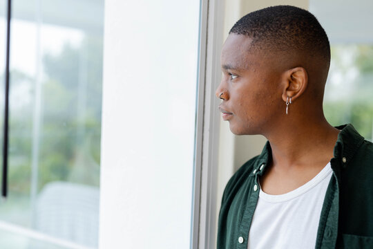 African American man standing, looking out glass window in dark-green shirt, hoops, copy space