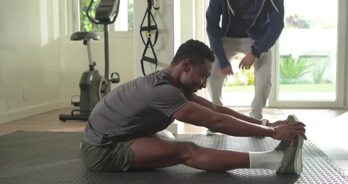 Mid Adult African American man stretching hamstring on home gym mat following trainer cues