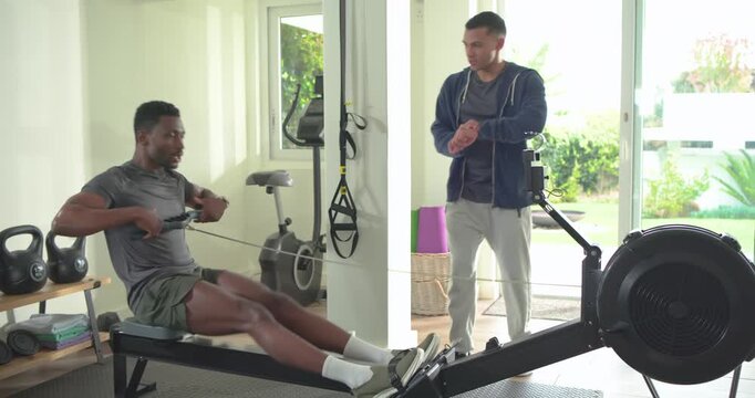 Coach entering home gym checking smartwatch coaching African American man rowing and offering water