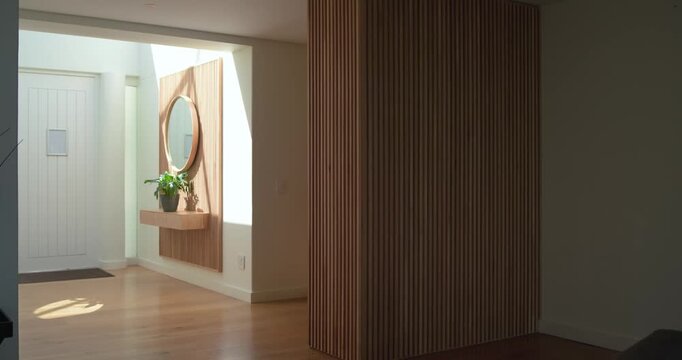 In entryway sunlight shifting through window is sliding light patch beside partition as day passes