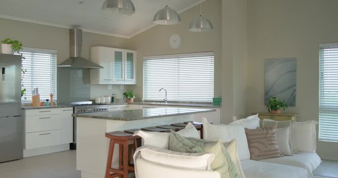 Camera is panning right revealing open-plan kitchen and living room while sunlight is casting light