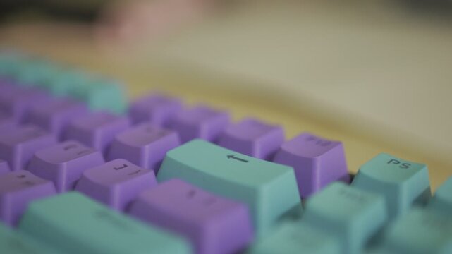 Close-up keyboard reveal vibrant purple and teal keys.  Focus shifts across the surface.  Gentle camera movement showcases detail.  Aesthetic appeal for tech, gaming, or design content