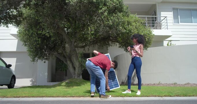 Asian man bringing solar panel, placing at curb for install while woman checking phone, copy space