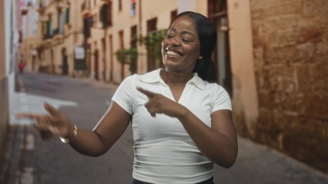 Woman pointing both index fingers like finger guns with bare arms, smiling broadly on a sunlit street; playful joy.