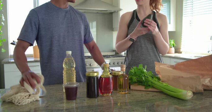 Diverse couple unpacking paper bag at kitchen island checking avocado and arranging celery for meal