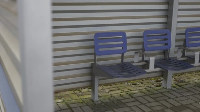 Panning shot reveals outdoor seating.  Metal chairs align with textured wall.  Focus shifts, showcasing structure detail.  Slow movement emphasizes architectural elements