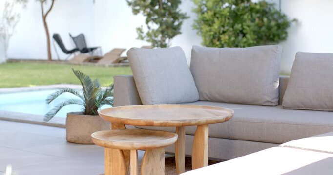 Camera is pushing in, making wooden nesting tables and sofa more prominent on patio for emphasis