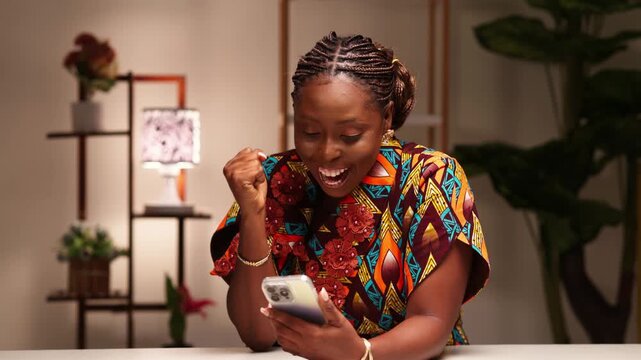 Cheerful young African woman celebrating while looking at smartphone, enjoying a win or victory