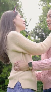 Vertical video: Meeting two women embracing and adjusting Merry tiara in park celebrating in knits