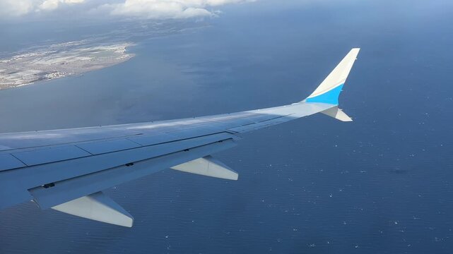 Airplane wing of Boeing 737 Max seen from a passenger window during a gentle banking turn above water approaching Gran Canaria Airport, smooth aerial travel footage
