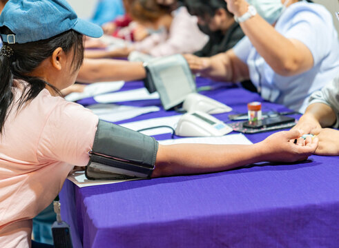 A row of people sitting at a long table undergoing blood pressure screenings.