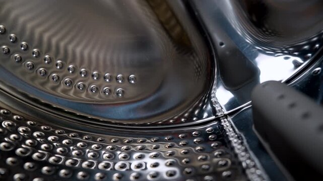 Washing machine drum close-up showing stainless steel interior of a modern washing machine. Household appliance, laundry concept, cleaning and hygiene background.