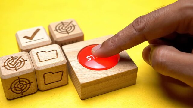 A finger pressing a red button on a wooden block with other blocks nearby on a yellow background