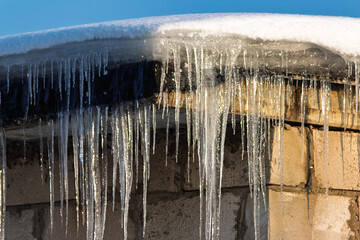 Sparkling icicles dripping from a snow-covered garage roof, illuminated by bright sunlight against a clear blue winter sky