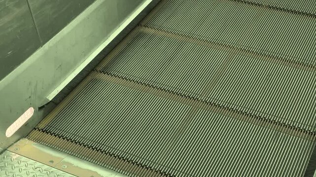 Close-up shot of escalator steps moving into the metal comb plate, ribbed treads sliding beneath brushed steel panels, emphasizing mechanical motion and industrial texture.