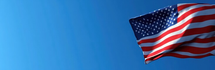 Obraz premium Waving American flag with stars and stripes against a clear blue sky, evoking pride and calm