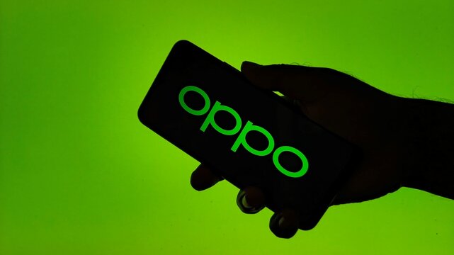 Hand holding Oppo smartphone against green background