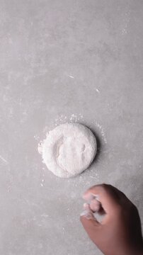 Overhead view of raw chinese scallion pancakes being rolled on grey countertop, top view of homemade scallion pancakes being shaped on countertop, process of making cong you bing