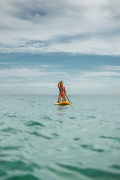 Female athlete enjoying paddle boarding on open sea. Summer sport activity, strong posture, freedom, adventure and wellness lifestyle surrounded by calm water and horizon