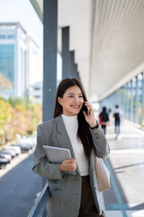 Fototapeta premium Asian woman student office worker talking on phone holding tablet as standing walking on footbridge.