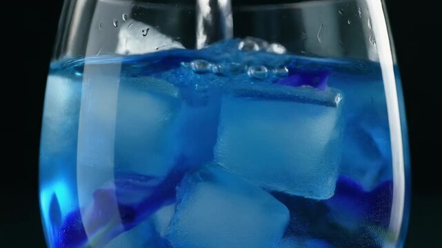 Pouring vibrant blue drink into glass with ice cubes and butterfly pea flower extract