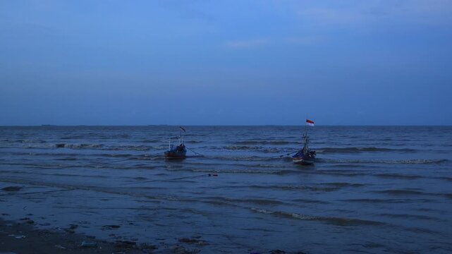 Two wooden fishing boats are anchored on the north coast of Tuban, East Java, Indonesia at dusk.