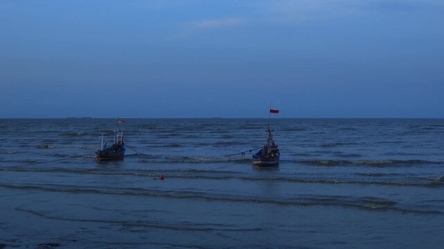Two wooden fishing boats are anchored on the north coast of Tuban, East Java, Indonesia at dusk.
