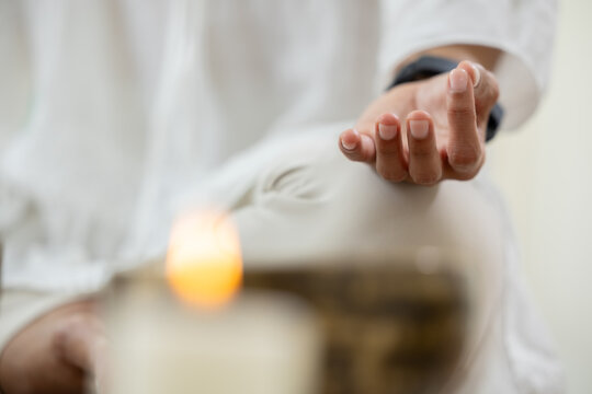 Mindful woman sitting white outfit holding hand gesture for deep sound healing meditation therapy session with tibetan singing bowl and candle creating peaceful calm relaxing energetic atmosphere