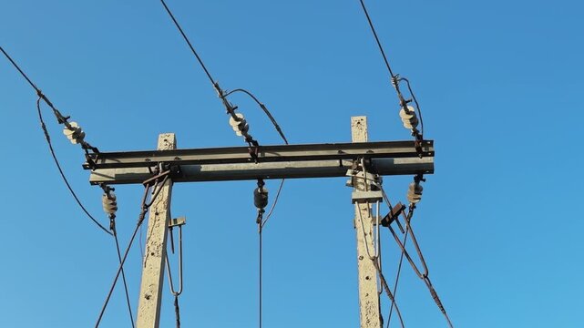 Static medium shot of a PSC or reinforced cement concrete power distribution pole in India, steel crossarm and ceramic insulators supporting low to medium voltage lines against a clear blue sky.