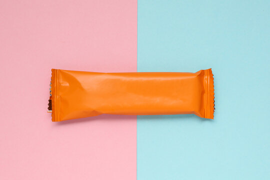 Chocolate bar pack mockup on pink blue background. Blank orange candy wrapper