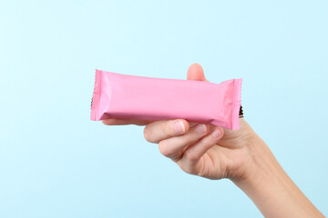 Hand holding Chocolate bar pack mockup on blue background. Blank pink candy wrapper