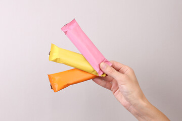 Obraz na płótnie Canvas Hand holding Chocolate bar packs mockup on gray background. Blank colored candy wrappers