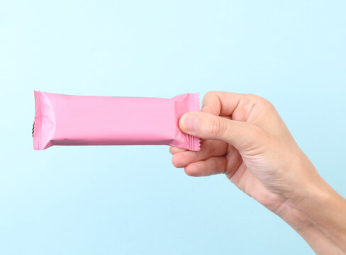 Hand holding Chocolate bar pack mockup on blue background. Blank pink candy wrapper