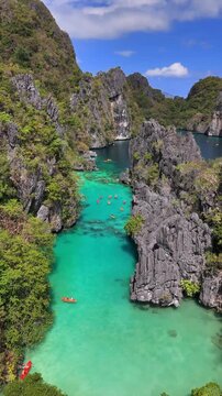 Scenic aerial View of Big Lagoon, with canoes, turquoise waters and rocky hllls around it with a blue sky day in Palawan, Philippines