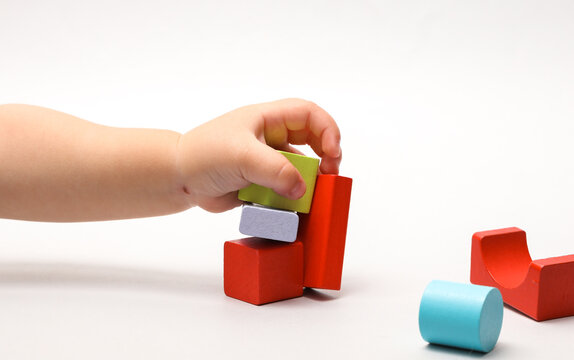 Baby's hands play with colorful wooden blocks of different shapes against a dark background. This is a developmental lesson in color recognition and the development of a baby's logic.