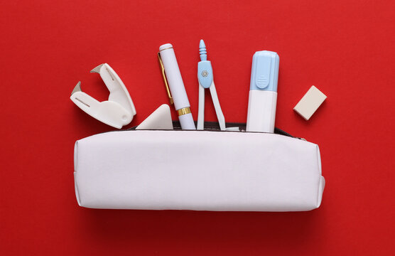 White pencil case mockup with school stationery supplies on red background. Flat lay. Top view
