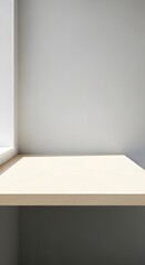 Fototapeta premium Empty light wooden tabletop against a minimalist white wall with natural light from a window, creating a clean background.