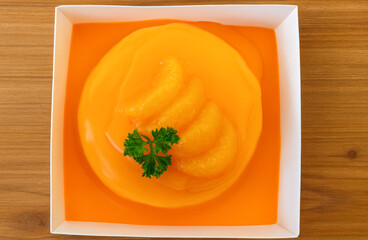 A bright orange gelatin dessert topped with mandarin slices and parsley sits elegantly in a white dish.