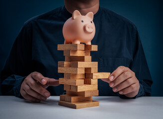 Concept of financial risk and investment strategy with piggy bank on unstable wooden blocks tower stacking game, representing fragile savings, economic uncertainty, and money management decisions.