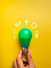 Green LED bulb held by hand on yellow background with eco icons. Minimal concept of energy saving, clean power, renewable energy, and sustainable technology for environmental-friendly innovation.