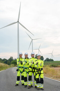 Caucasian adult engineer team standing together on road inside wind farm confident teamwork after renewable electricity generation project clean energy technology green power industry safety uniform
