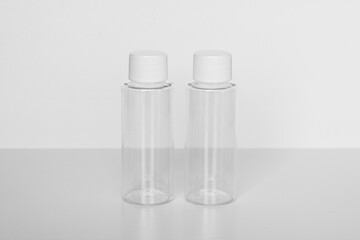 Two empty transparent plastic bottles with white caps isolated on a white background. Minimalist cosmetic or toiletry packaging mockup for a duo of liquid beauty products.