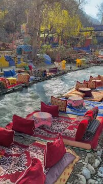 Cinematic 4K Vertical of traditional Moroccan riverside seating with carpets in Ourika Valley, Atlas Mountains.