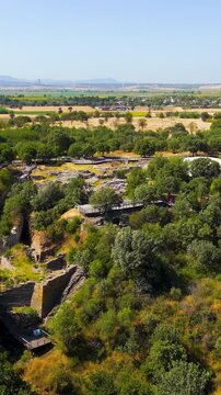 Vertical video. Tevfikiye, Turkey. Aerial view of the Pillar House and other freestanding structures of Troy VI, their stone foundations surrounded by green. Aerial view, Departure of the camera. Ric