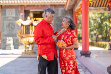 Naklejka premium Happy senior asian couple holding mandarin oranges and incense sticks at Chinese temple, Elderly husband and wife celebrating Lunar New Year, worship, traditional culture and retirement concept