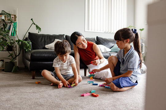 Two children seated on carpeted floor playing with blocks with mum nearby in living room